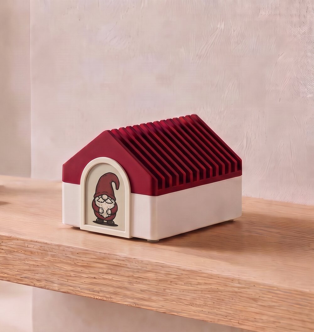 Tomte Tom, a small house-shaped device with a red gable roof, sitting on a wooden shelf.